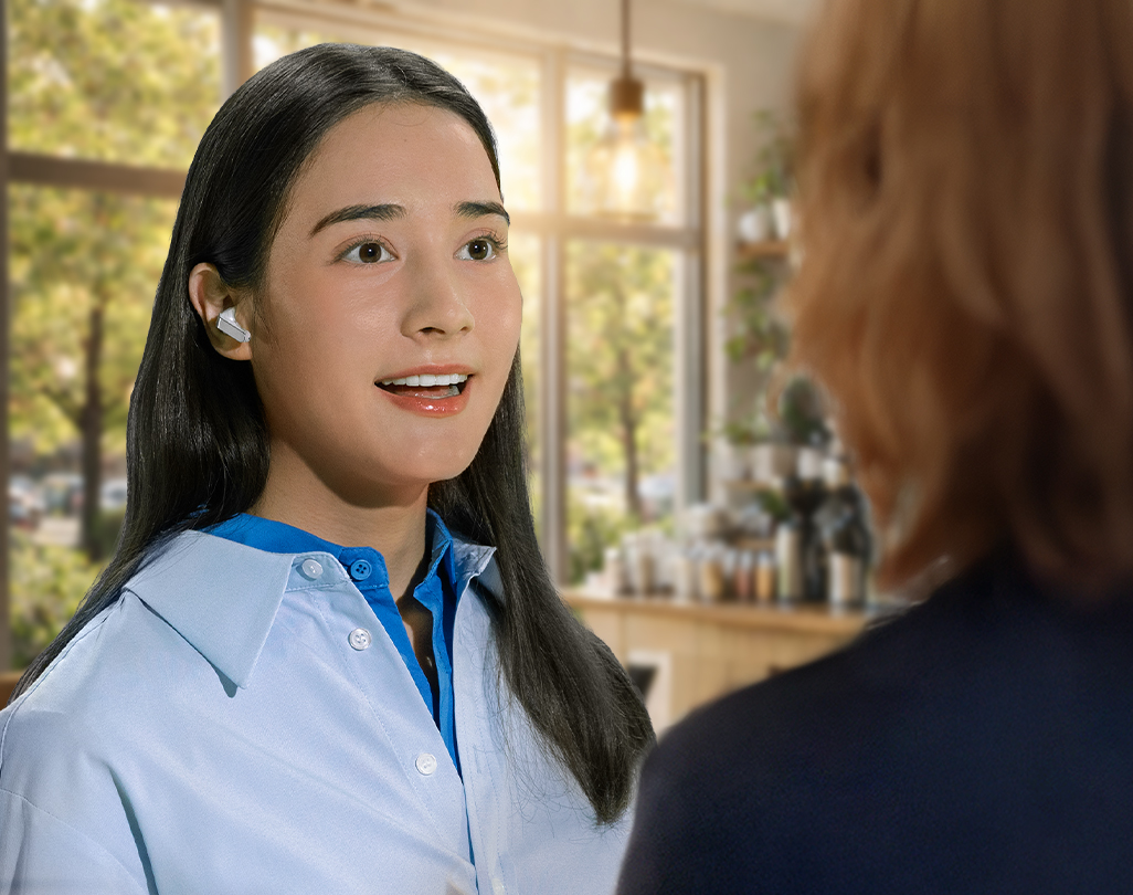 A woman using a single, white Galaxy Buds4 Pro while holding a conversation with another person, showcasing the Voice Detect feature.